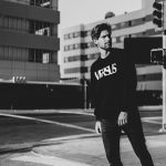 Stylish man in black outfit poses confidently at Los Angeles intersection, capturing urban street style.