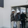 A group of diverse clients with a realtor at a new construction site entrance.