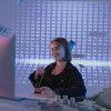 Smiling woman surrounded by digital and physical currency in a tech office setting.