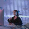 Smiling woman surrounded by digital and physical currency in a tech office setting.