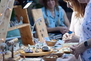 Shoppers browse handcrafted jewelry at an outdoor artisan market stall.