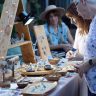 Shoppers browse handcrafted jewelry at an outdoor artisan market stall.
