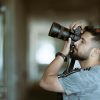 A focused photographer taking a photo with precision indoors, wearing casual attire.