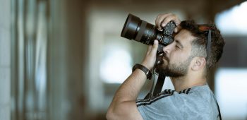A focused photographer taking a photo with precision indoors, wearing casual attire.