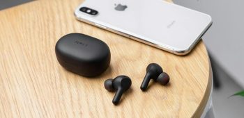 Close-up of modern gadgets: wireless earphones and a smartphone on a sleek wooden table.