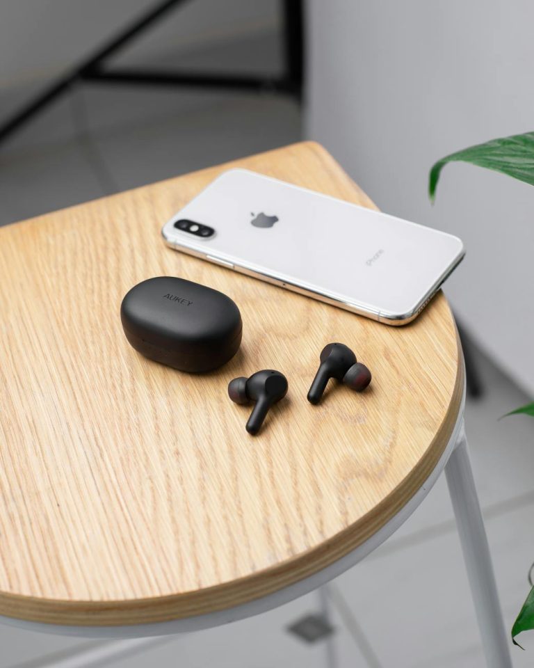Close-up of modern gadgets: wireless earphones and a smartphone on a sleek wooden table.