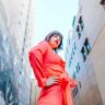 Model in vibrant orange attire poses confidently in an urban setting with graffiti.