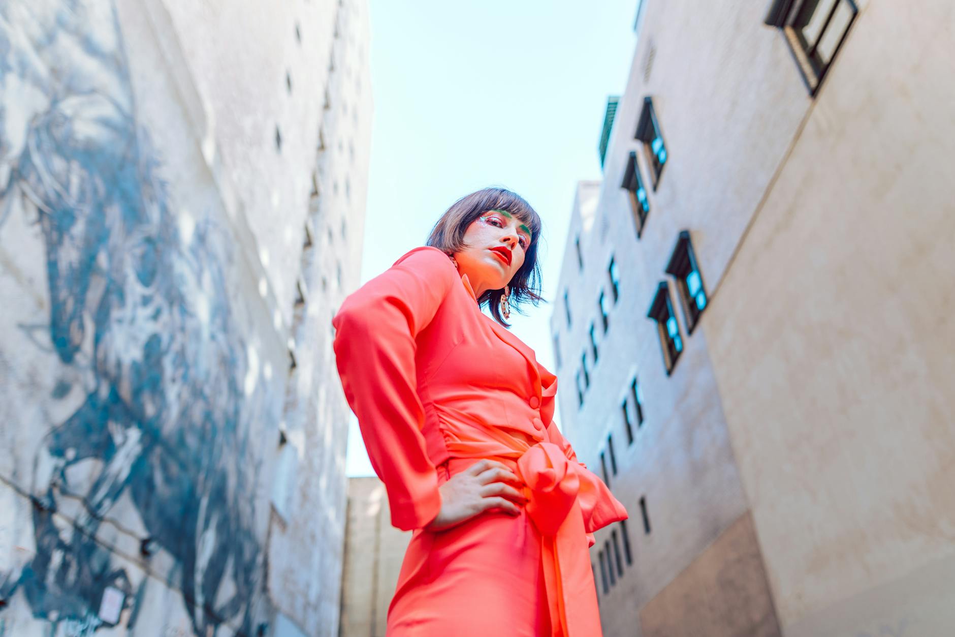 Model in vibrant orange attire poses confidently in an urban setting with graffiti.