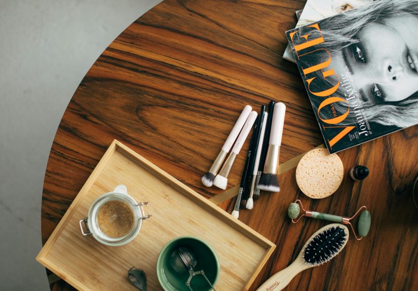 Stylish flatlay featuring makeup brushes, a Vogue magazine, and a coffee cup on a wooden table.